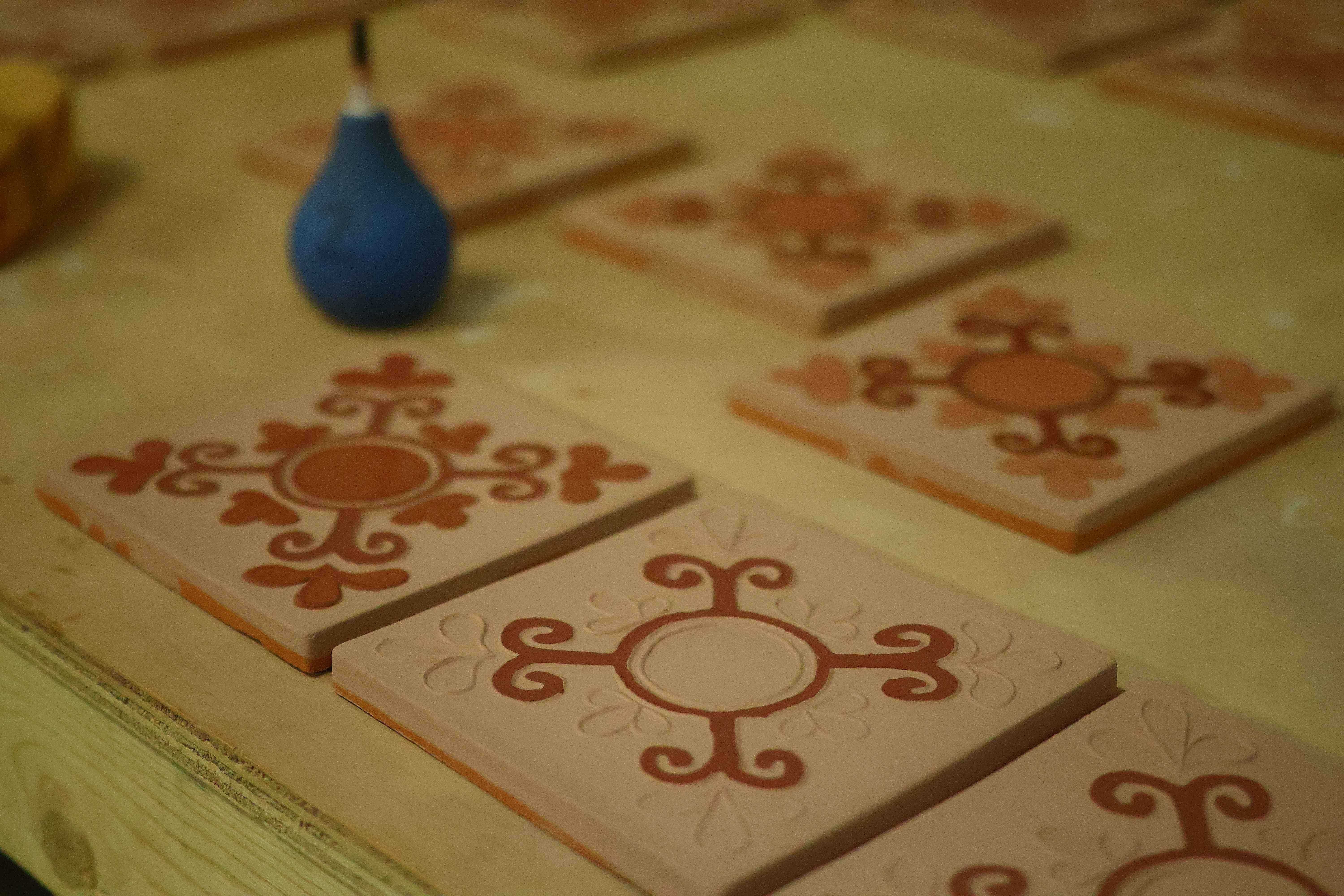 Carved terracotta Courtyard tiles laid across the studio bench beside a blue glazing bulb