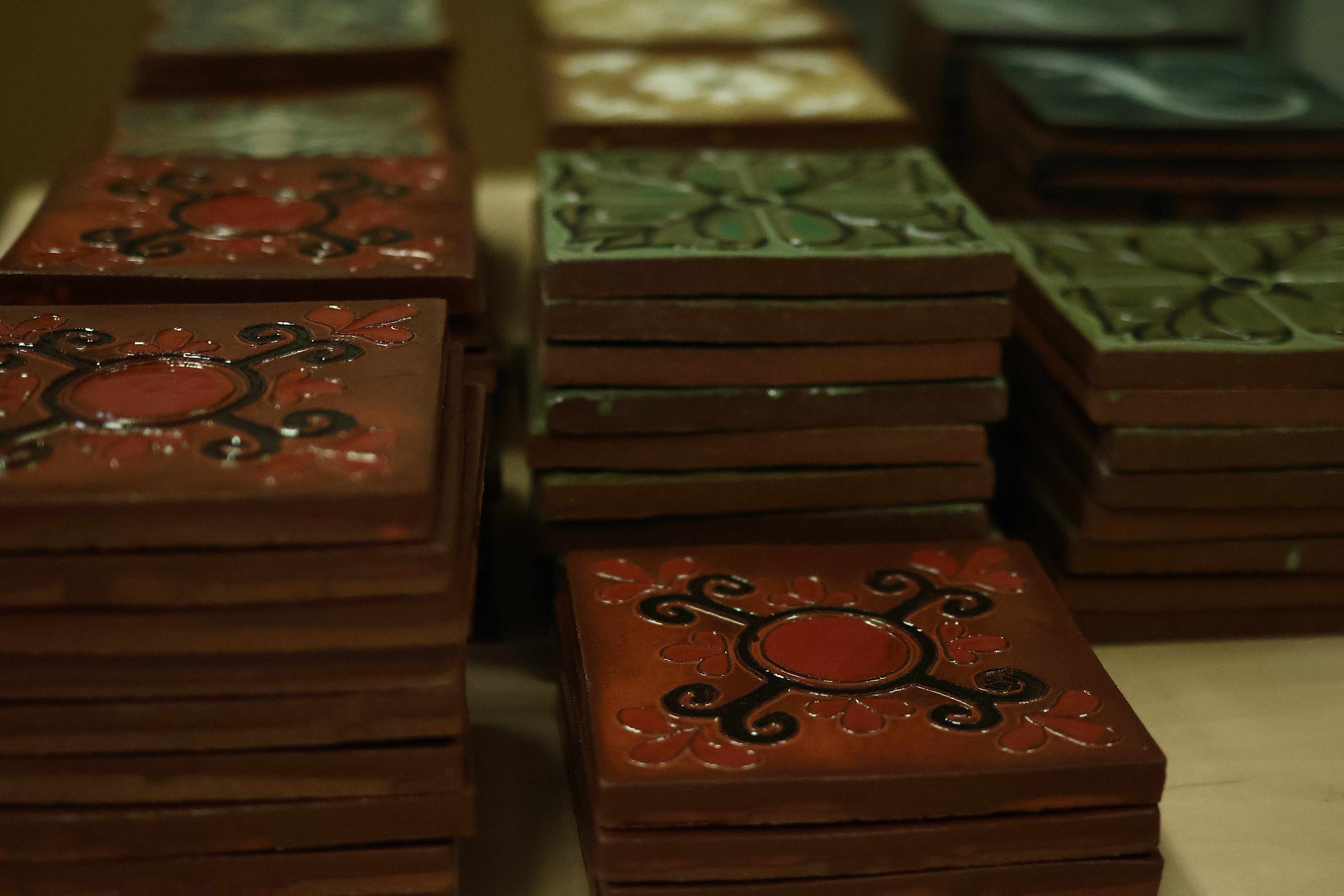 Stacks of finished Courtyard Series tiles — terracotta tiles with red medallion and black scroll motifs beside green floral tiles