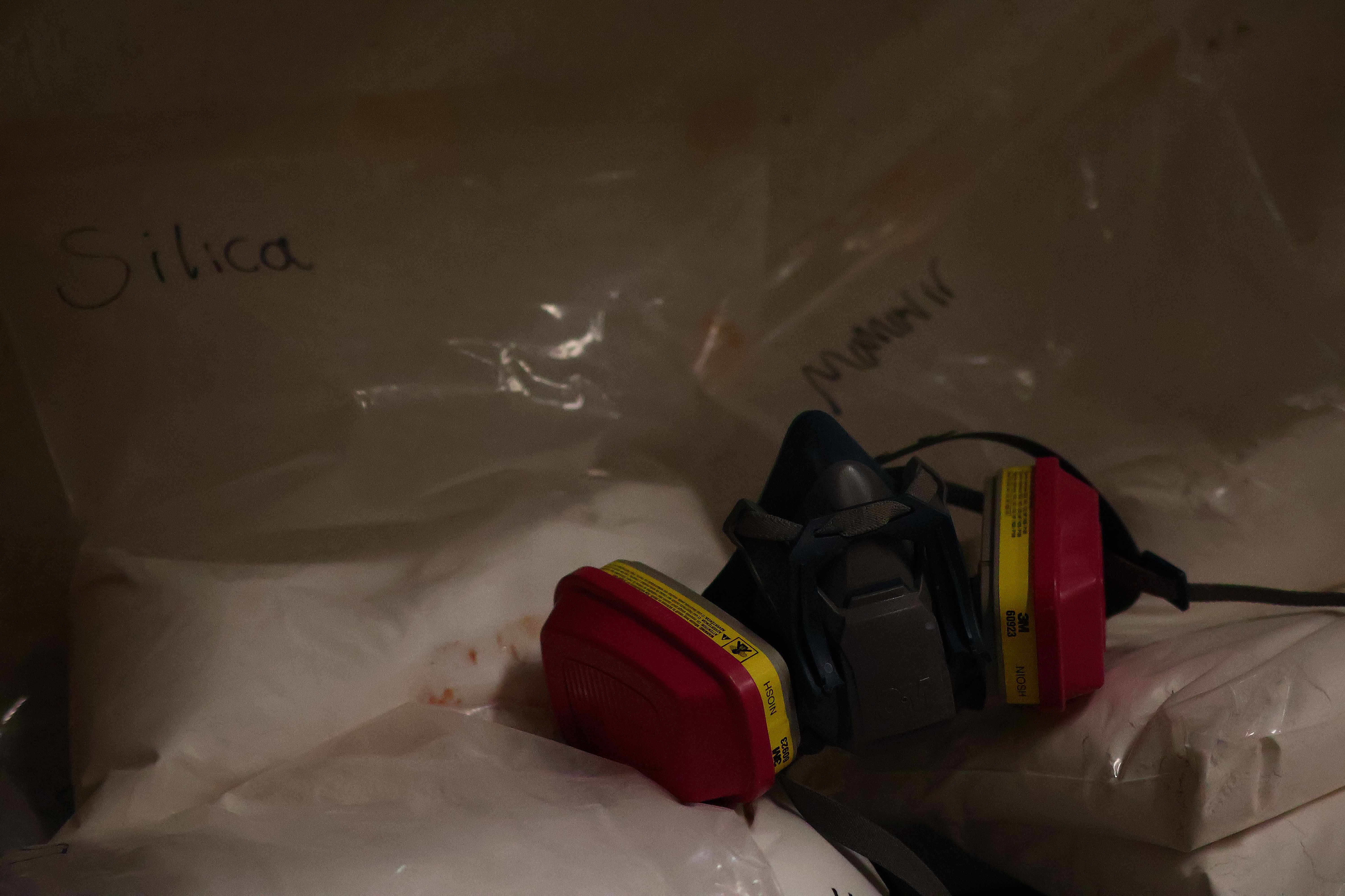 A 3M respirator mask resting on bags of raw material labeled Silica in the studio