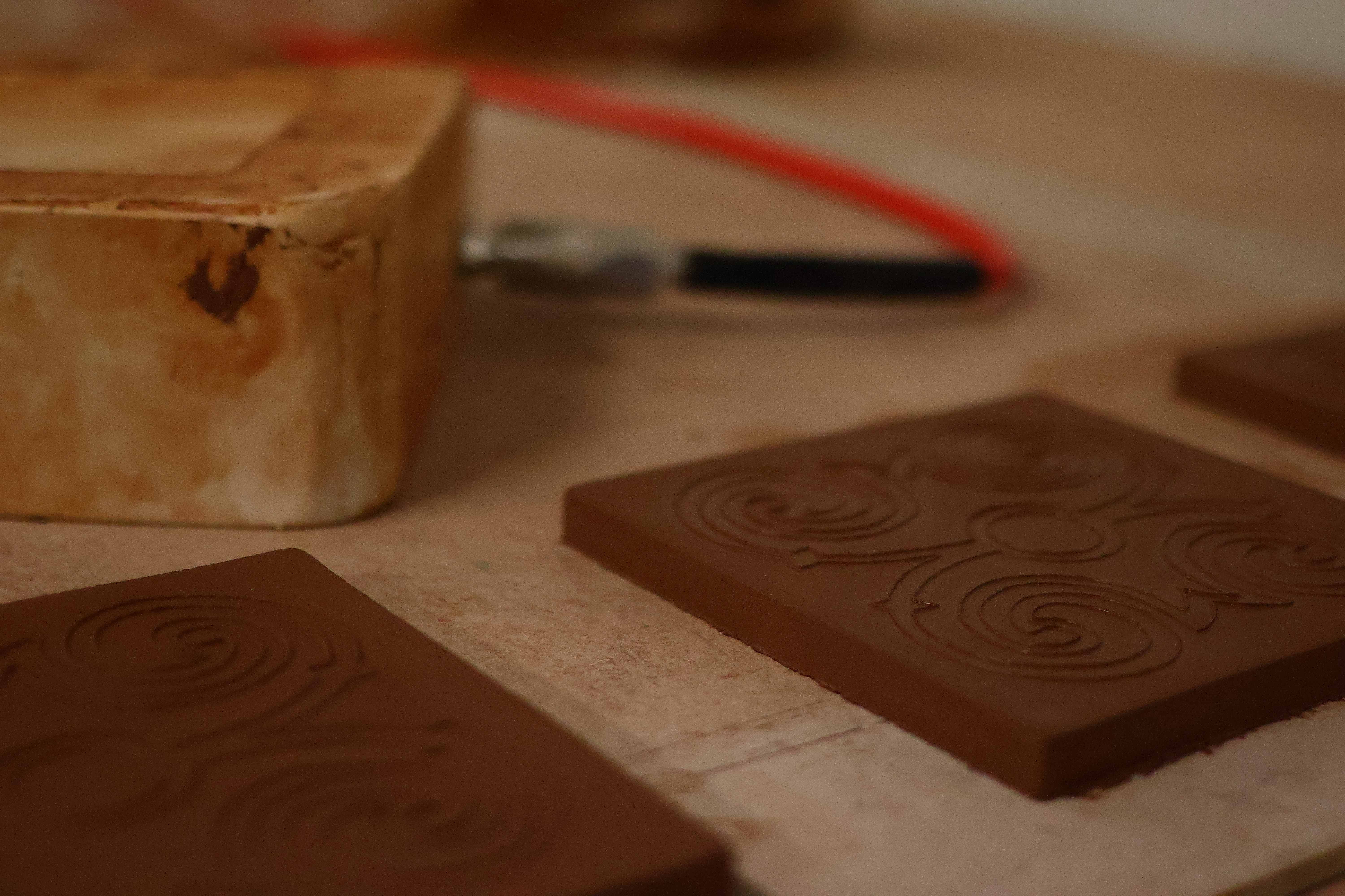 A plaster stamp mold beside terracotta tiles carved with spiral scroll relief